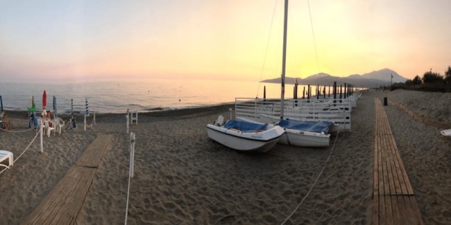 Spiaggia al tramonto con barche a vela sulla sabbia.