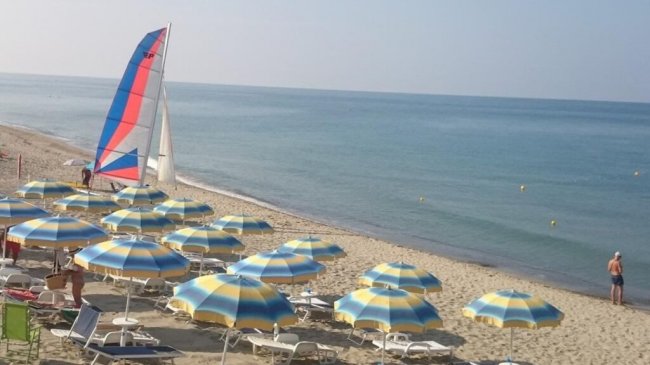 Ombrelloni e barca a vela su spiaggia sabbiosa.
