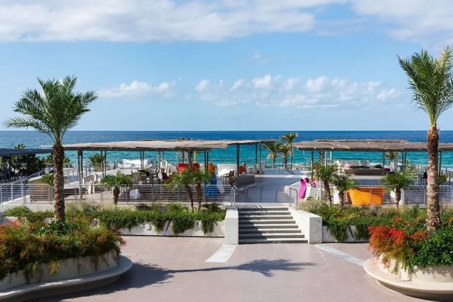 Terrazza vista mare con palme e salotti.