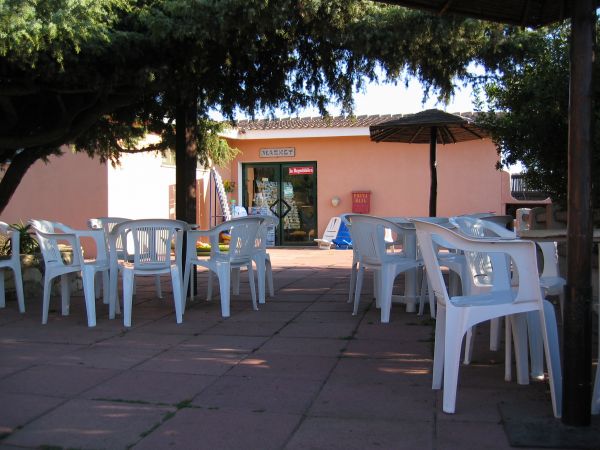 Tavoli bianchi di plastica all'aperto davanti a un edificio rosa con un'insegna.