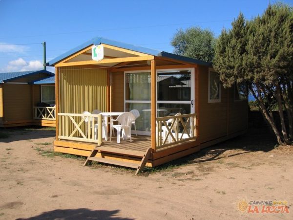 Bungalow in legno con veranda e mobili da esterno, situato in un ambiente naturale con cielo sereno.