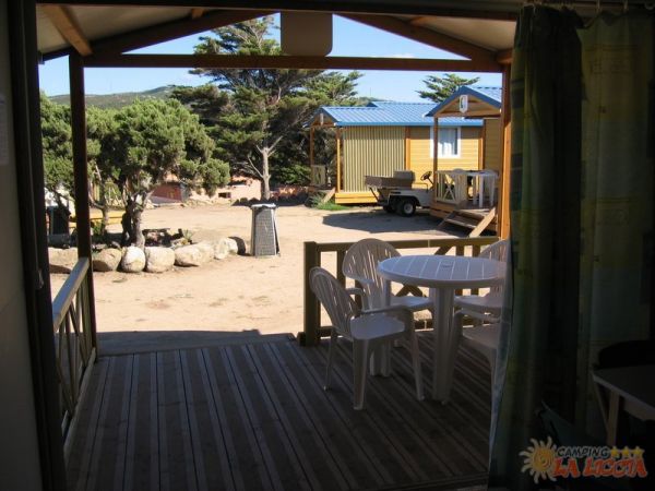 Vista dalla veranda verso altri chalet, con tavolo e sedie bianche.