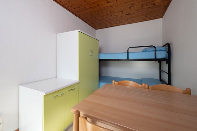 Letto a castello, armadio verde e tavolo di legno.