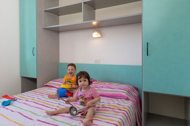 Due bambini giocano su un letto a righe colorate.