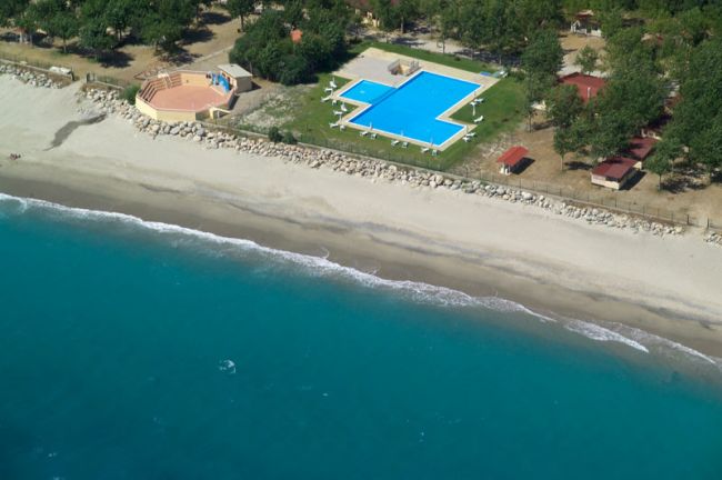 Piscina a forma irregolare vicino alla spiaggia sabbiosa con mare blu.