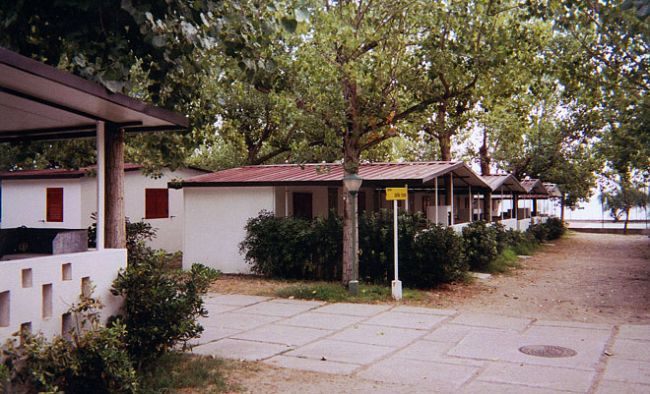 Bungalov in fila con tetti rossi sotto alberi in un'area turistica.