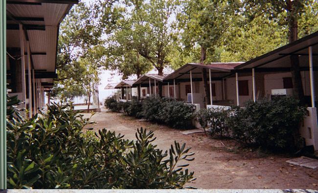 File di bungalow bianchi con tetti scuri e vegetazione.