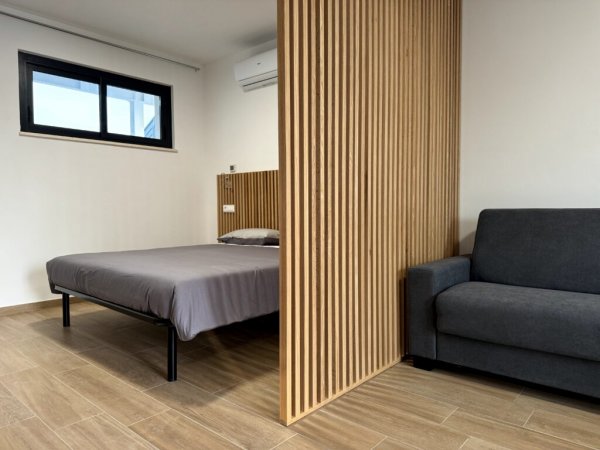 Camera con letto, separé in legno e divano grigio.