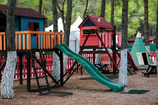 Area giochi con scivoli e casette colorate tra gli alberi.