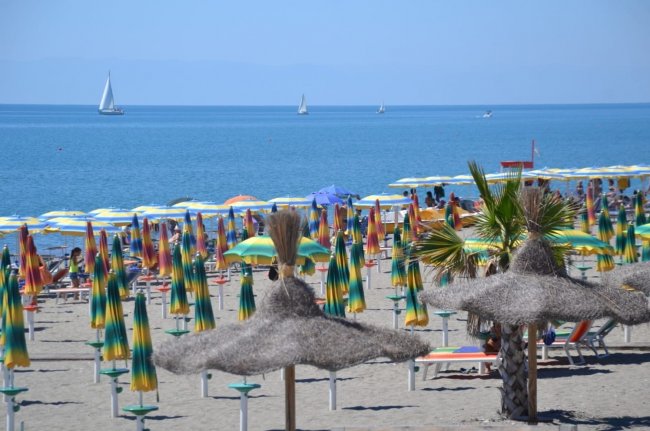Spiaggia con ombrelloni colorati e barche a vela in mare.