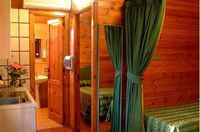 Interno di una stanza in legno con lavandino e letto, separati da una tenda verde.