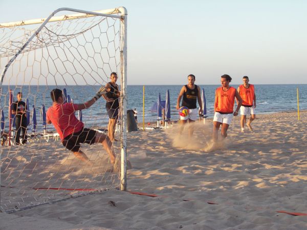 Partita di calcio sulla spiaggia, un giocatore calcia il pallone verso la porta.