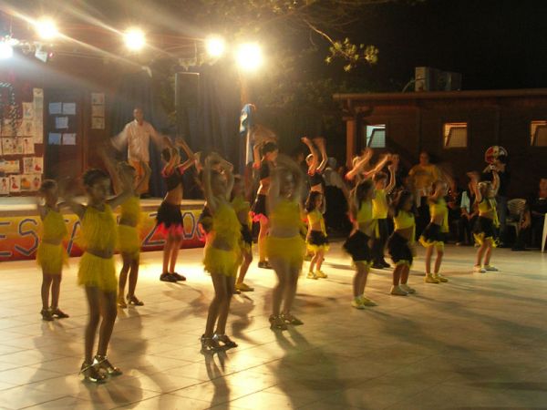 Bambini in costume giallo e nero che ballano su un palco illuminato la sera.