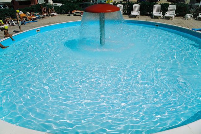 Piscina rotonda con una fontana centrale e sedie a sdraio tutt'intorno.