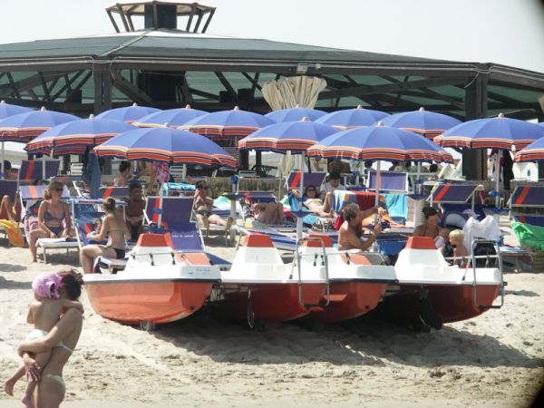 Spiaggia con ombrelloni blu, sdraio e pedalò rossi.