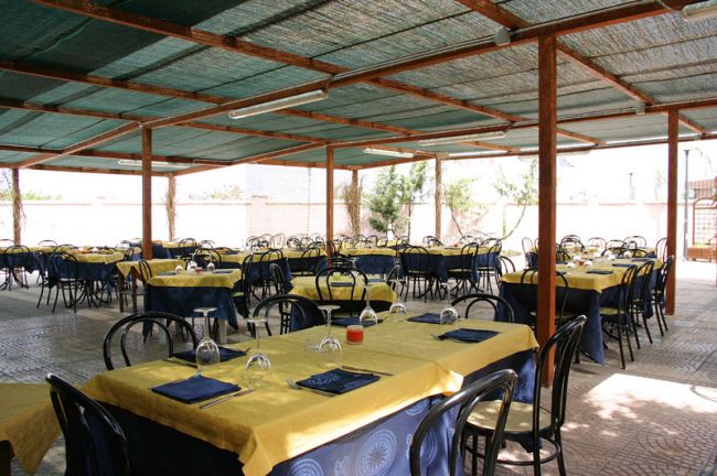 Sala da pranzo con tavoli apparecchiati e sedie nere, coperta da un pergolato.