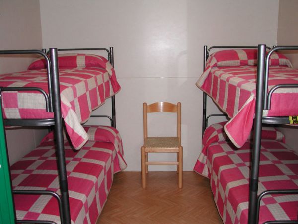 Due letti a castello con coperte a quadri rossi e bianchi; una sedia di legno al centro.