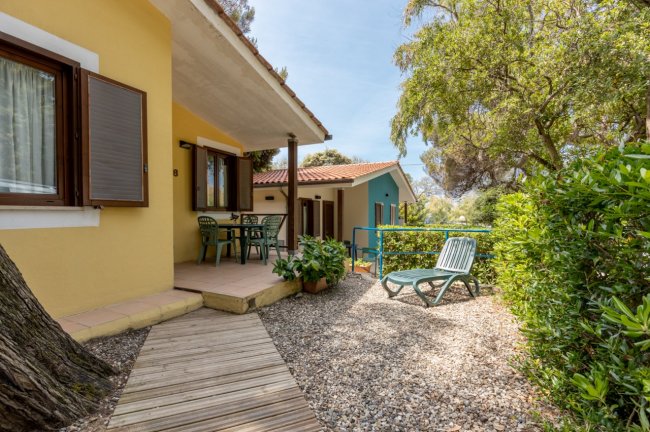 Bungalow giallo con veranda e sedie da giardino.