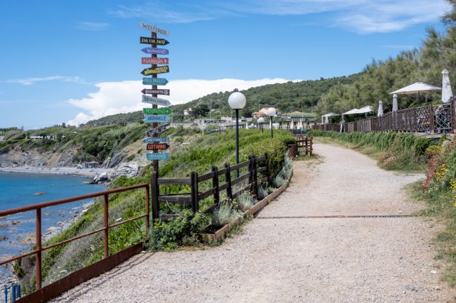 Sentiero lungo la costa con cartelli colorati e lampioni.