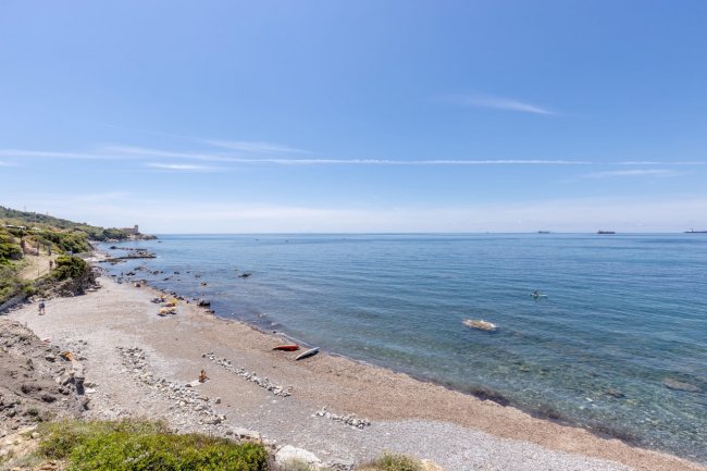 Spiaggia rocciosa con mare calmo all'orizzonte.