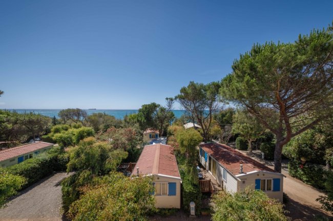 Case mobili tra alberi, vista mare in lontananza.