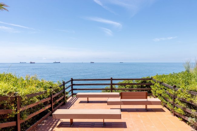 Panchine su terrazza con vista mare e navi in lontananza.