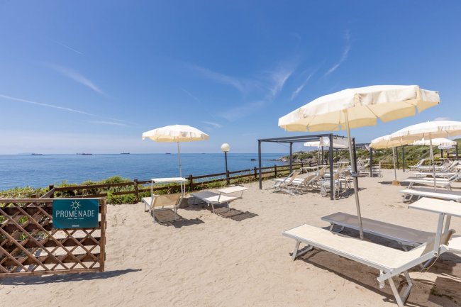 Spiaggia sabbiosa con ombrelloni bianchi e vista mare.