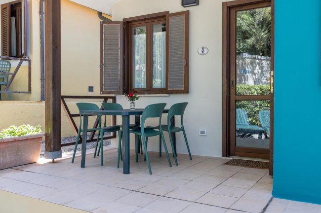 Patio esterno con tavolo e sedie verdi.