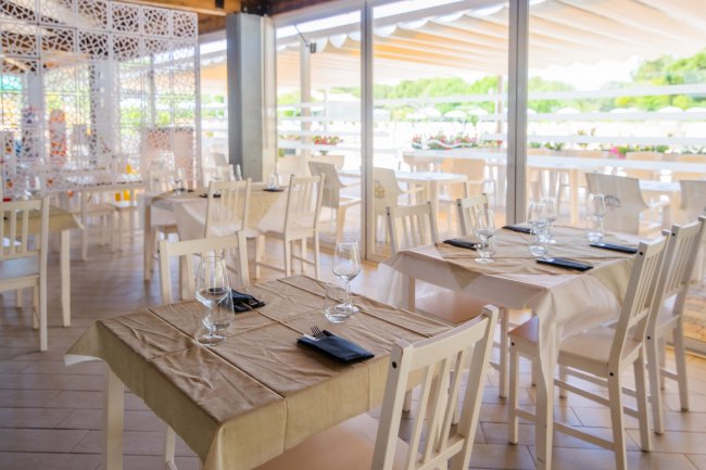Ristorante con tavoli apparecchiati, vista esterna verso la piscina e il giardino.