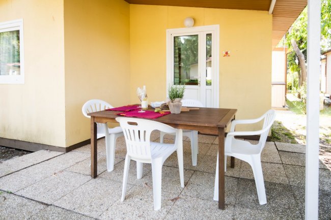 Tavolo da pranzo all'aperto con sedie bianche su una terrazza piastrellata.