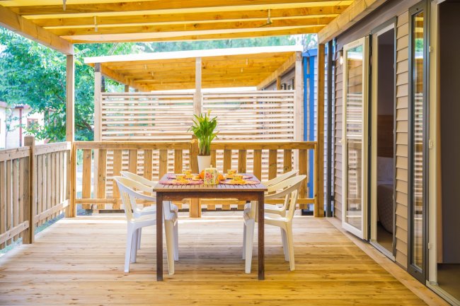 Terrazza in legno con tavolo da pranzo, sedie bianche e decorazioni floreali.