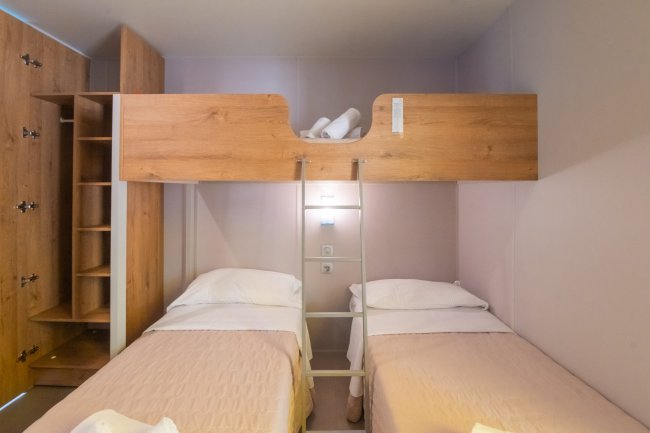 Due letti singoli con soppalco in legno e scala centrale, armadio aperto.