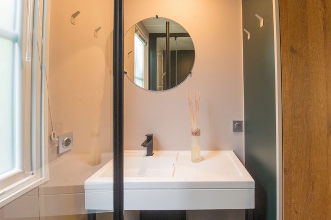 Bagno con specchio rotondo sopra un lavandino bianco e un diffusore di oli essenziali.