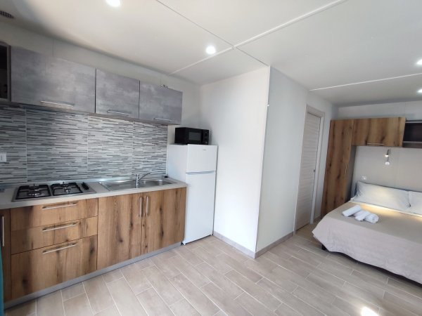 Monolocale con cucina moderna, frigorifero, microonde e letto matrimoniale con asciugamani.