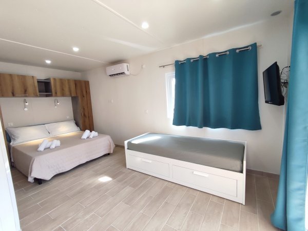 Camera con letto matrimoniale, divano letto singolo, tende blu e TV a parete.