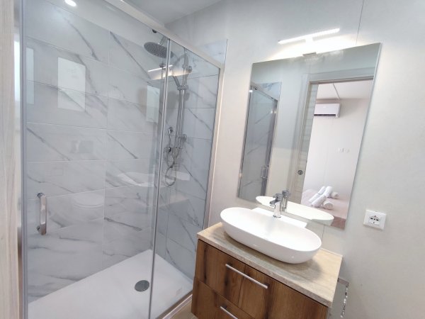 Bagno moderno con doccia in vetro e lavabo su mobile in legno, specchio ampio.