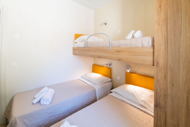 Camera con due letti singoli e letto a castello, testiere arancioni e asciugamani piegati.