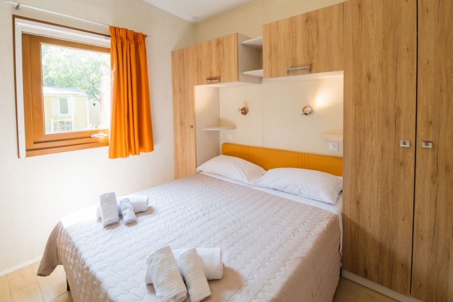Camera da letto con letto matrimoniale, armadio in legno e finestra con tende arancioni.