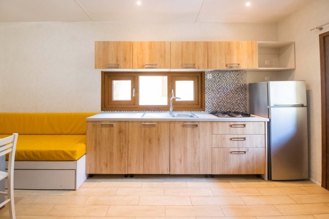 Cucina moderna con mobili in legno chiaro, frigorifero e panca con cuscini gialli.