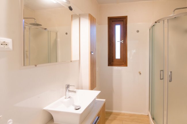 Bagno con doccia, lavandino e finestra stretta.