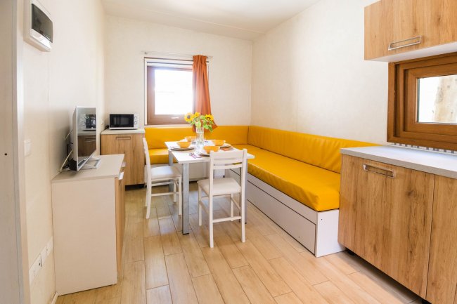 Cucina con divano giallo, tavolo bianco e mobili in legno.