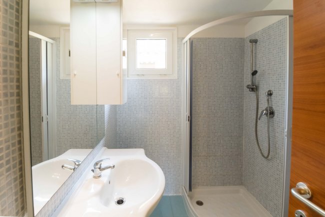 Bagno moderno con doccia, lavabo doppio e piccolo finestrino.