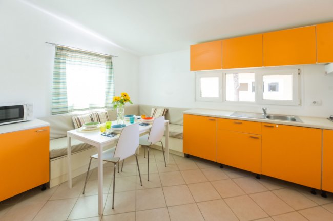 Cucina luminosa con mobili arancioni, tavolo da pranzo e seduta angolare.