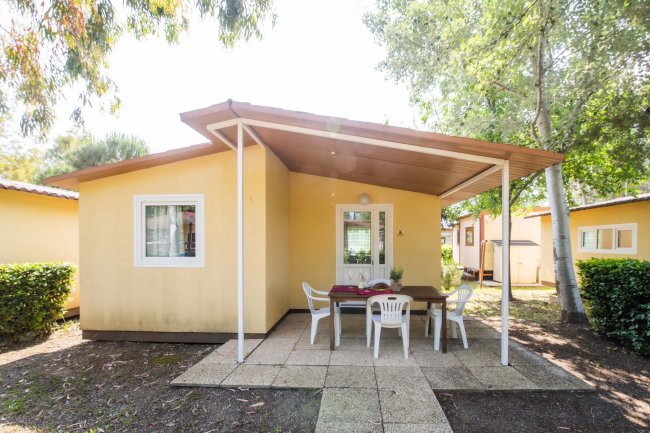 Una casa gialla con patio coperto, tavolo e sedie di plastica all'esterno.