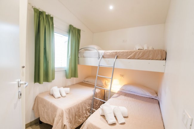 Camera con due letti singoli, uno a castello. Tende verdi e asciugamani piegati sul letto inferiore.