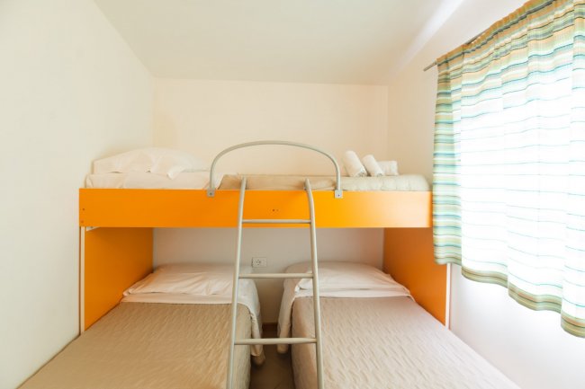 Camera con due letti singoli, uno a castello. Tende a righe e asciugamani sul letto inferiore.