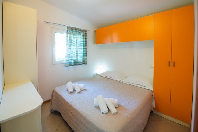 Camera con letto matrimoniale, armadio arancione e tende a righe. Asciugamani piegati sul letto.