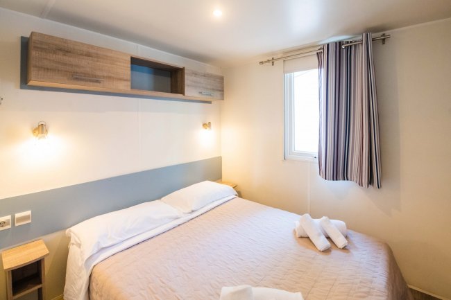 Camera da letto con letto matrimoniale, lenzuola chiare e asciugamani piegati.