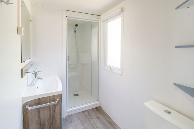 Bagno moderno con doccia in vetro, lavabo e pavimento in legno chiaro.