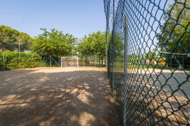 Campo sportivo con porta da calcio e recinzione, ombreggiato da alberi.